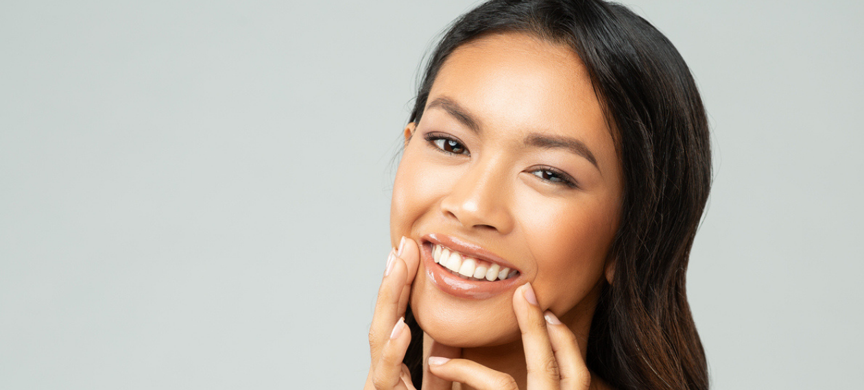 smiling woman with dark hair resting her hand near her face against a gray background