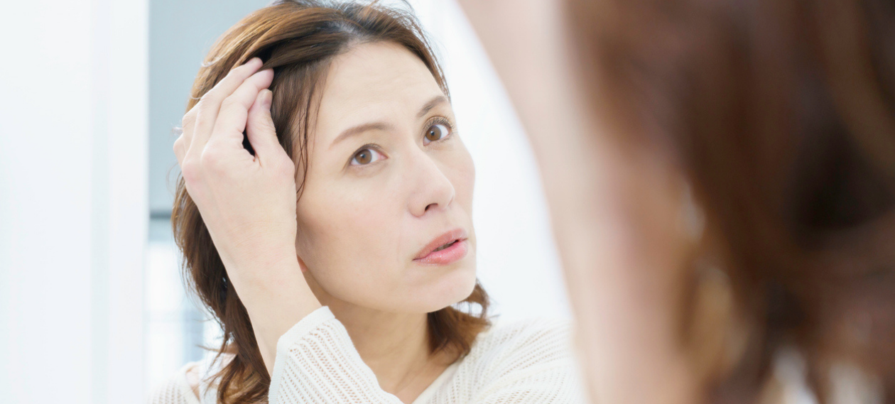 woman lifting her hair to look at her forehead and hairline in the mirror