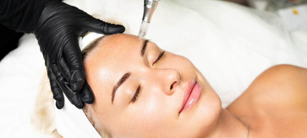 woman with a white head wrap receiving a facial treatment from a gloved provider